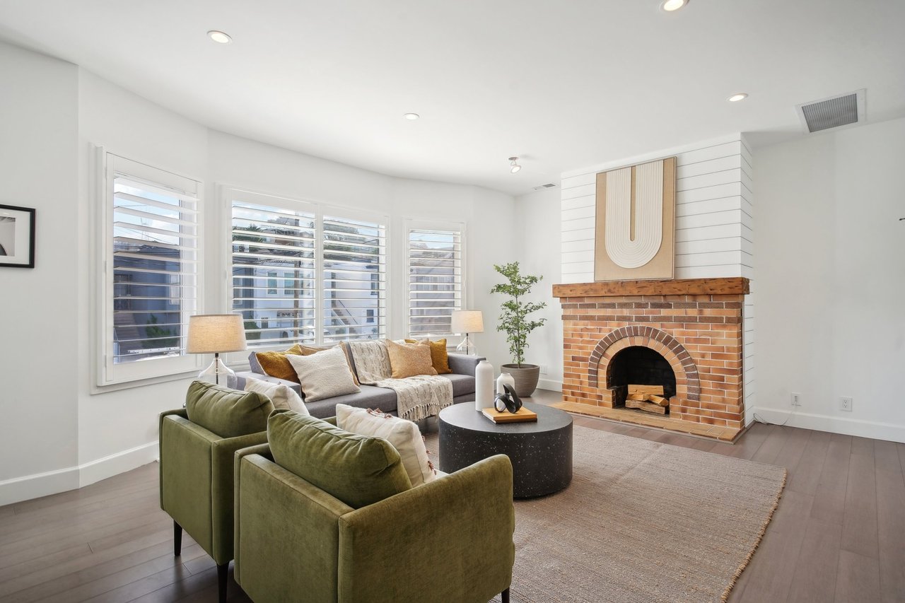 A cozy living room with a brick fireplace, a gray sofa, and two green armchairs.
