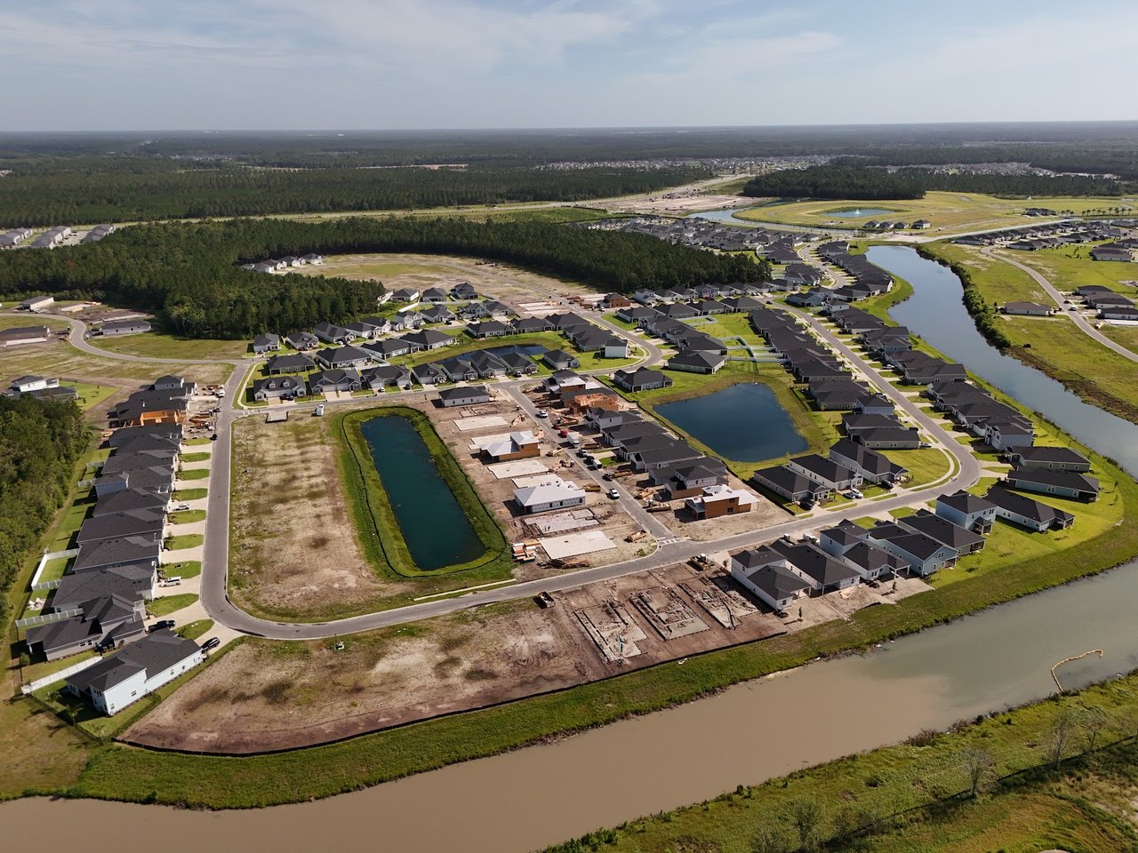 Aerial view of a residential community with homes under construction, ponds, and a winding waterway.