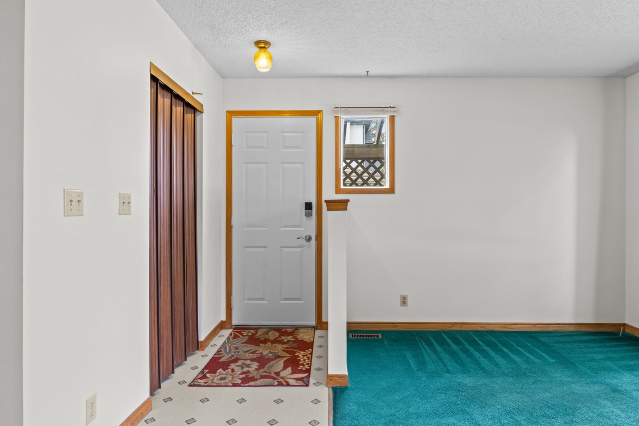 Empty entryway with a gray front door, folding closet doors, patterned tile, and teal carpet.