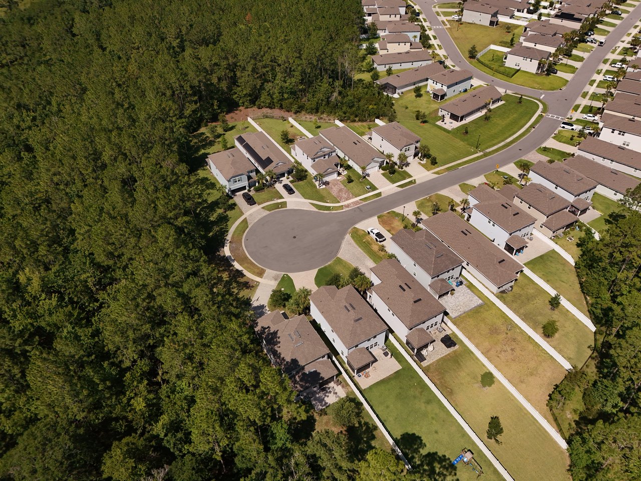 Aerial view of homes along a cul-de-sac beside dense woods.