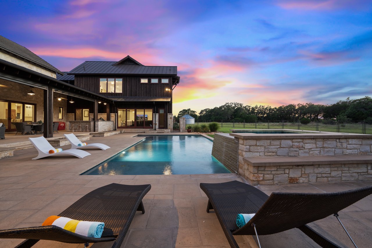 Twilight view of the pool and spa at 335 Winning Colors, Key Ranch at the Polo Club, built by Elite Pools of Dripping Springs, with a stone patio and lounge seating.