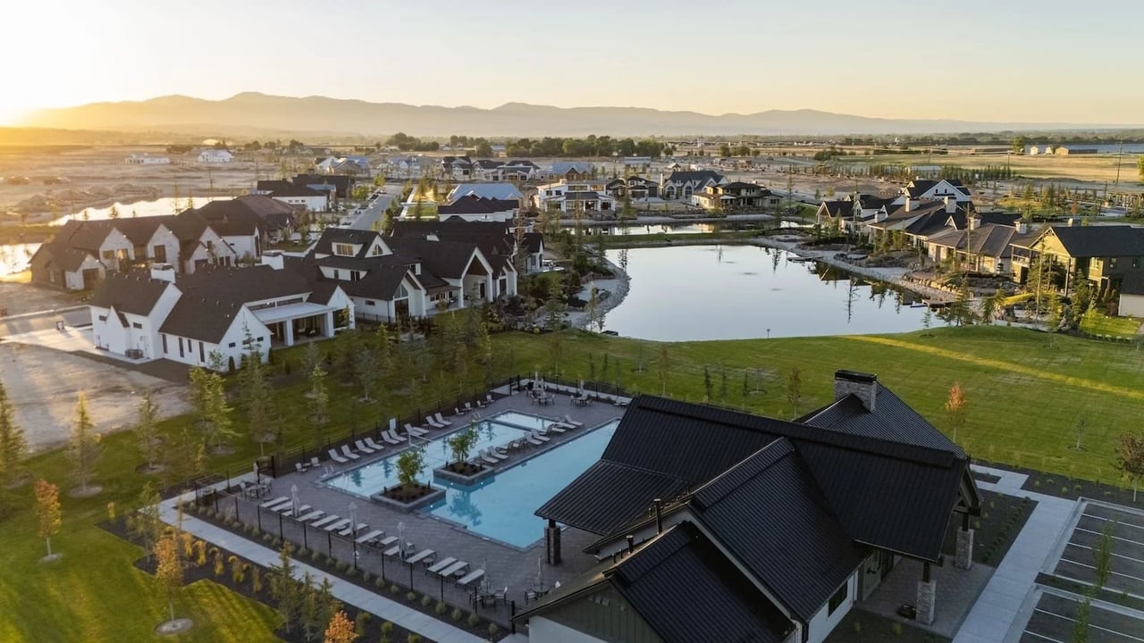 Aerial view of homes around a pond, with a community pool and distant mountains.