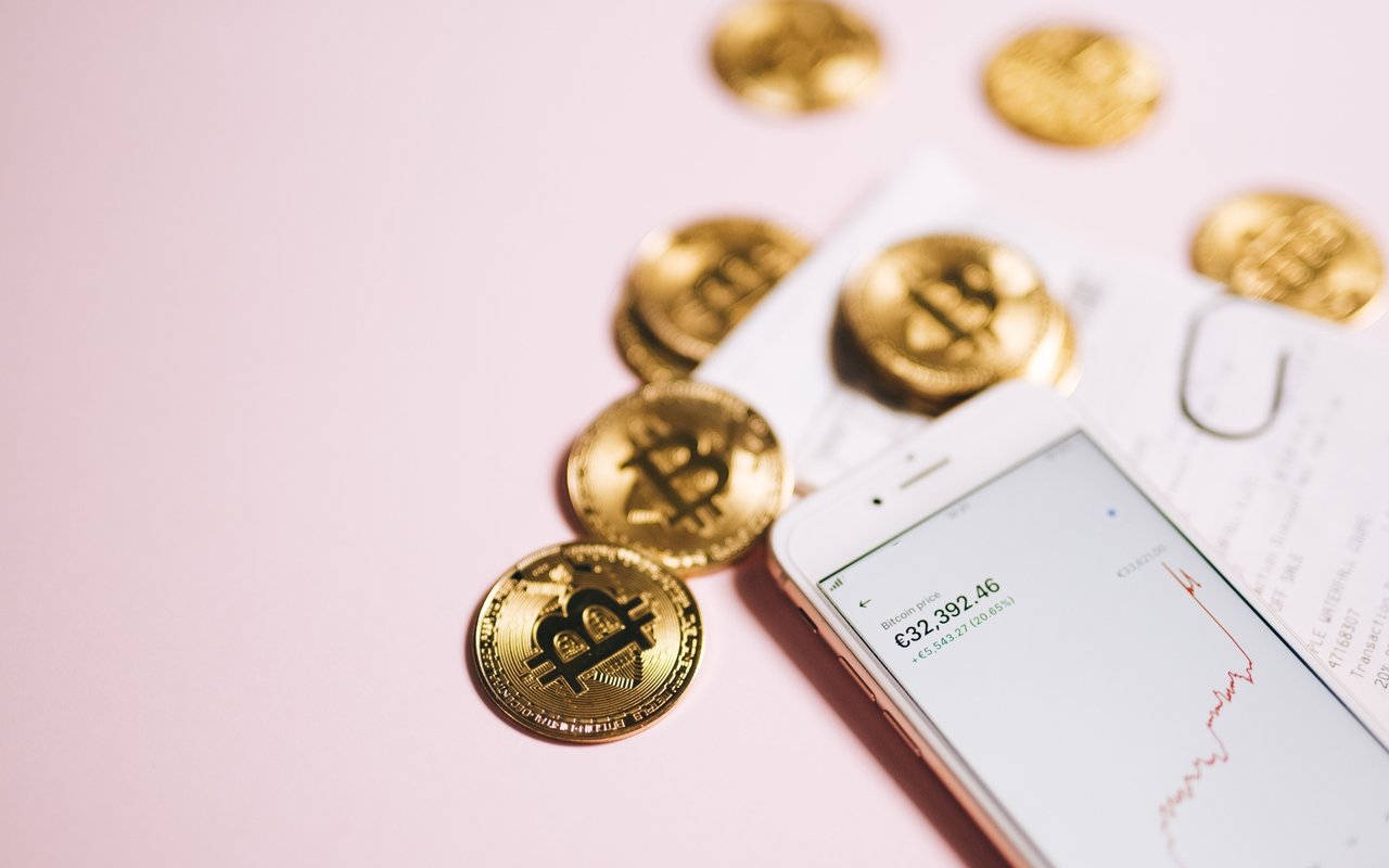 Bitcoin tokens beside a smartphone showing a rising price chart.