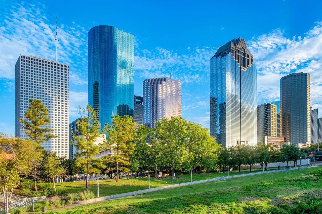 Downtown Houston skyline rising above a green park beneath a blue sky.