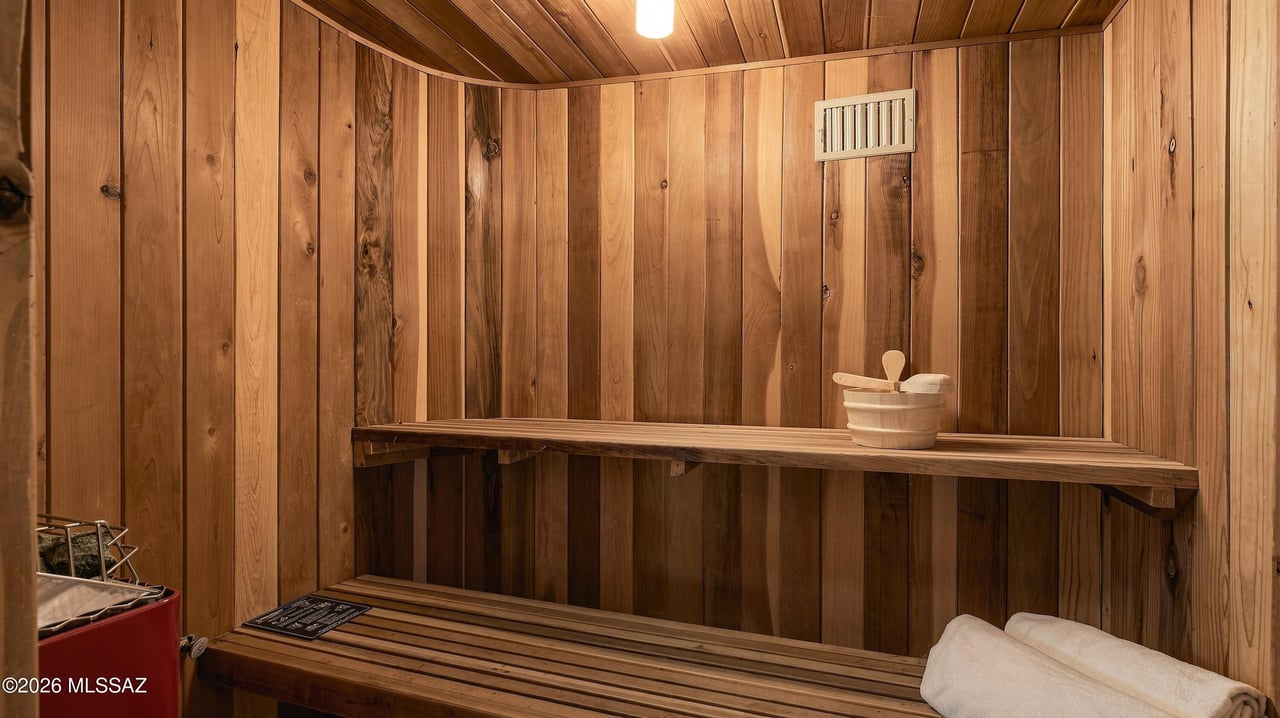 Wood-paneled sauna with tiered benches, a heater, a bucket and ladle, and folded towels.