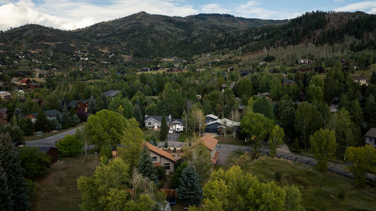 Aerial view of homes among trees, with forested mountains in the background.