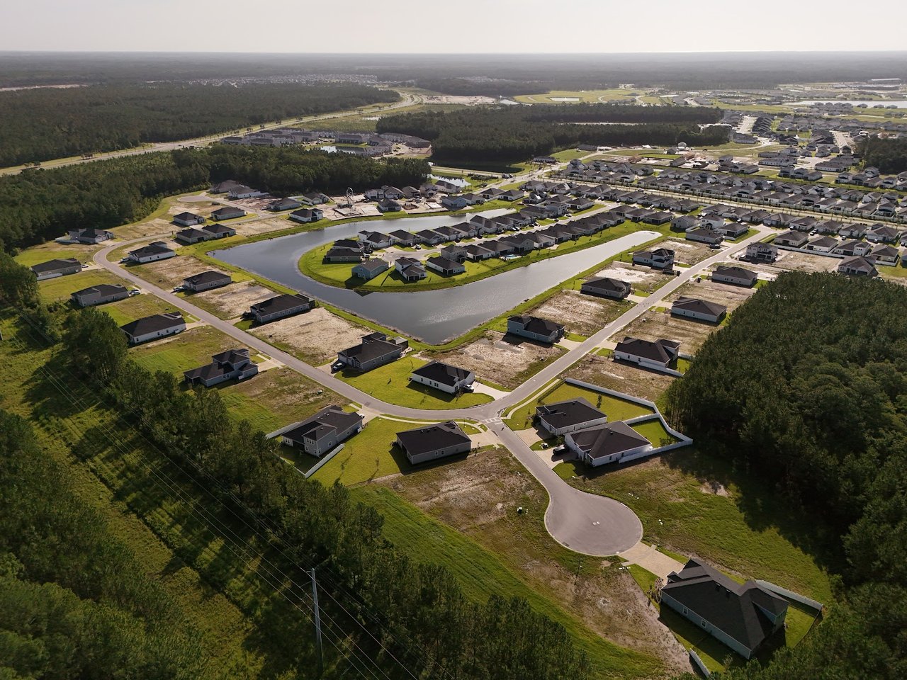 Aerial view of a new subdivision with homes, vacant lots, and a winding pond.