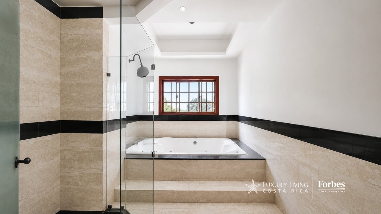 Bathroom with a built-in jetted tub beneath a wood-framed window and a glass-enclosed shower.