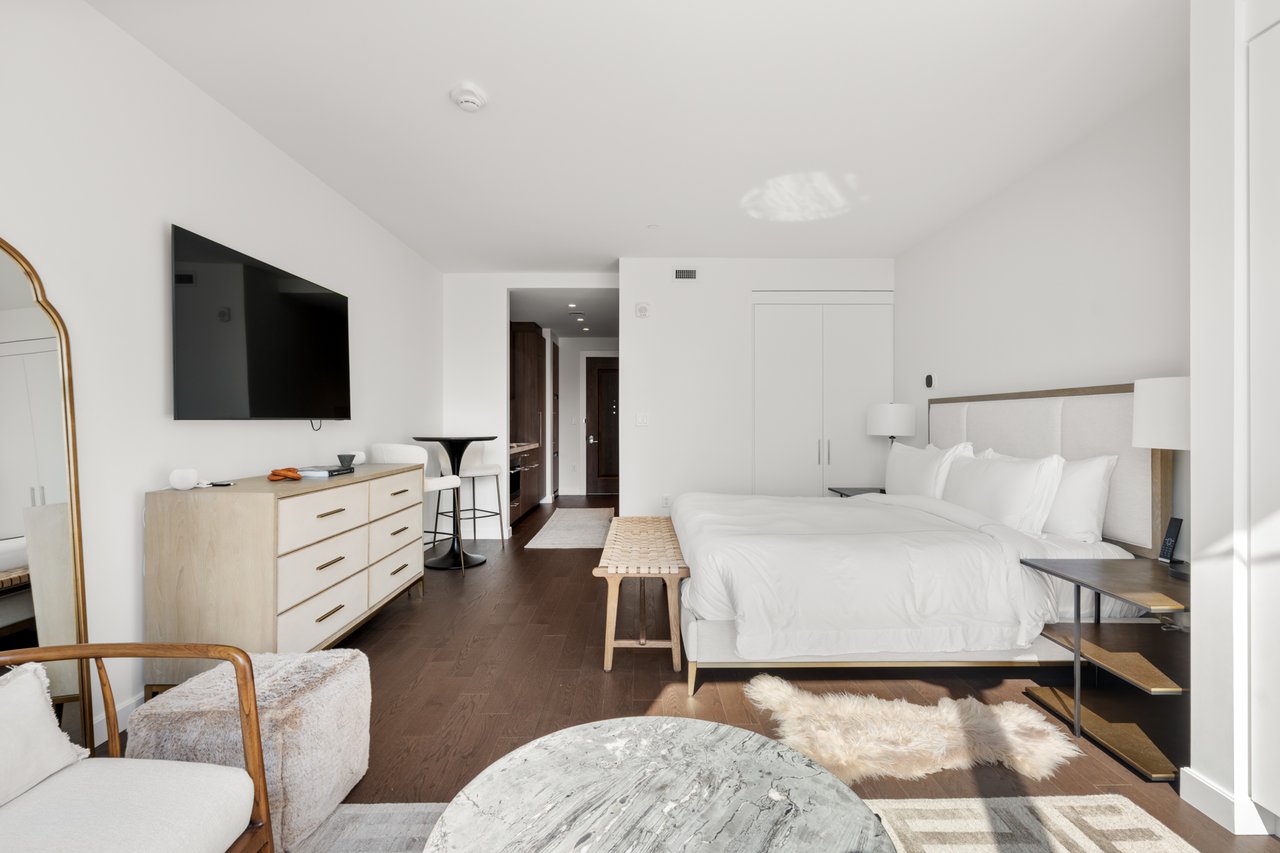 Furnished bedroom with a king bed, wall-mounted television, wood flooring, and a small sitting area.