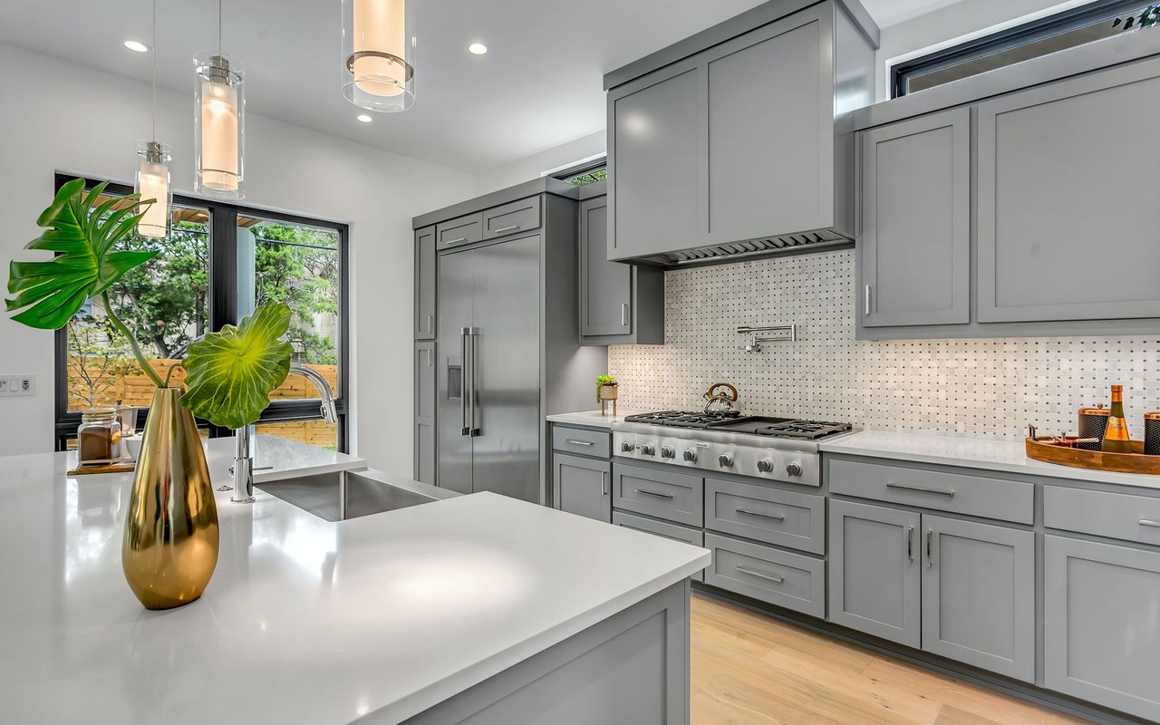 Modern gray-and-white kitchen with a large island, stainless appliances, and windows overlooking greenery.