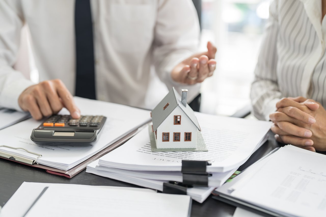 Close-up of hands and documents with miniature house model during real estate consultation.
