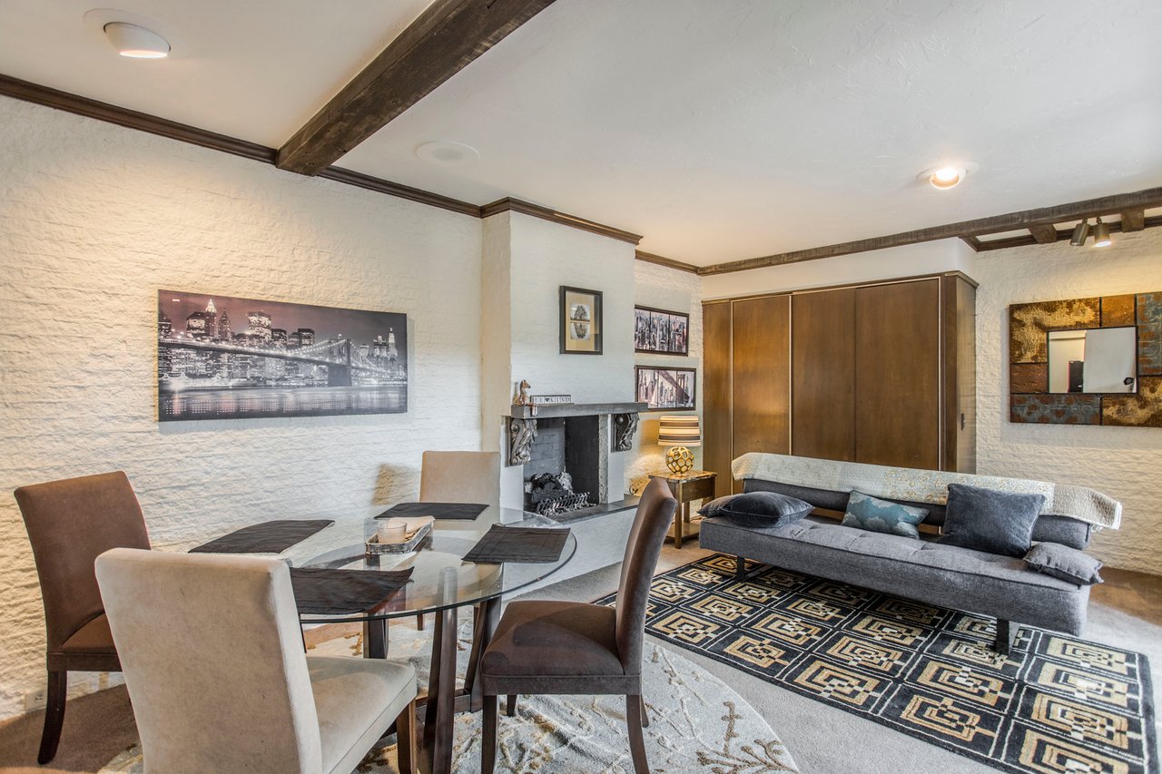 Living room with a stone fireplace, exposed wood beams, and an adjoining dining area.