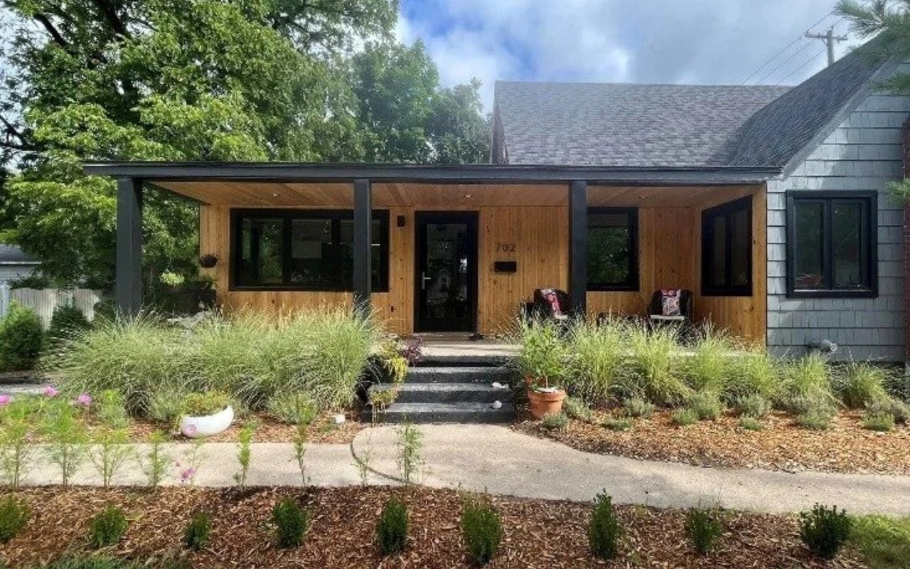 Renovated house with a wood-clad front porch, dark-framed windows, and landscaped garden beds.