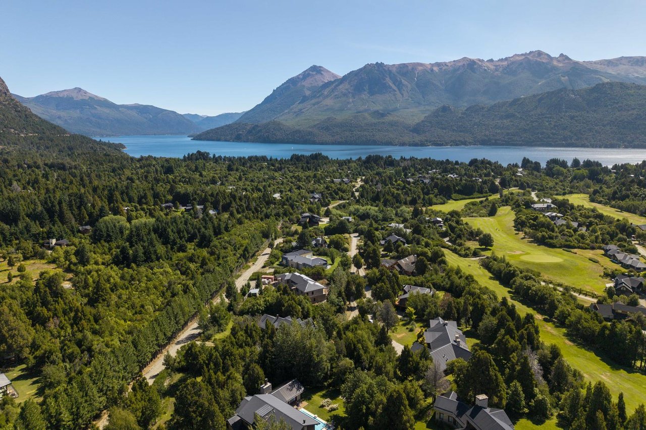 Aerial view of homes and a golf course beside a lake, with forested mountains beyond.