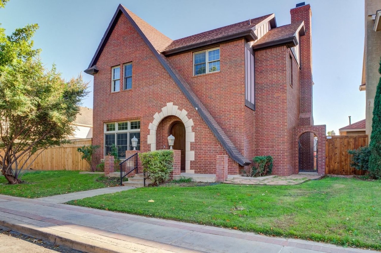 Two-story red brick house with steep gables, an arched entry, and a front lawn.