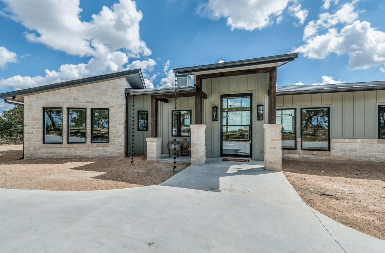 Modern single-story home with pale stone facade, dark wood entry framing, and an unfinished yard.