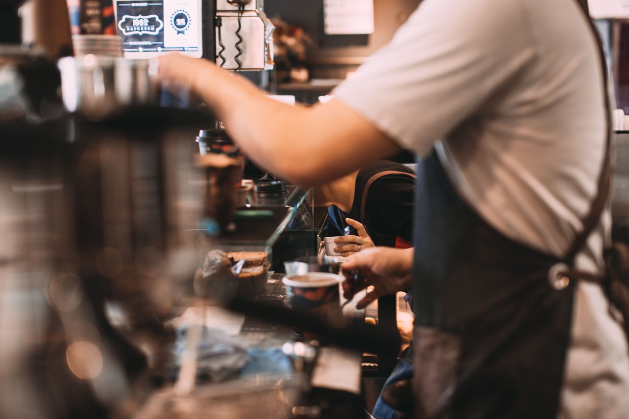 Barista preparing coffee drinks behind a café counter.