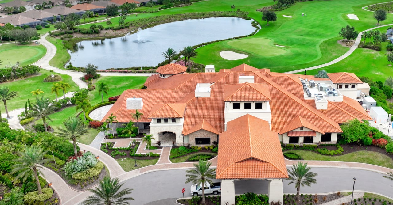 Aerial view of a red-tile-roof clubhouse beside a golf course and pond
