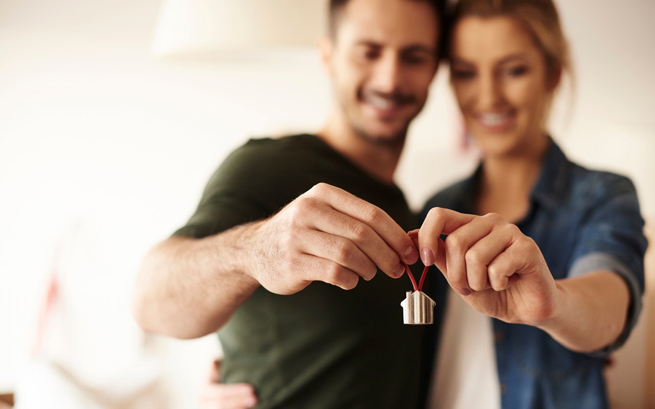 A smiling couple holds a small house-shaped charm together.