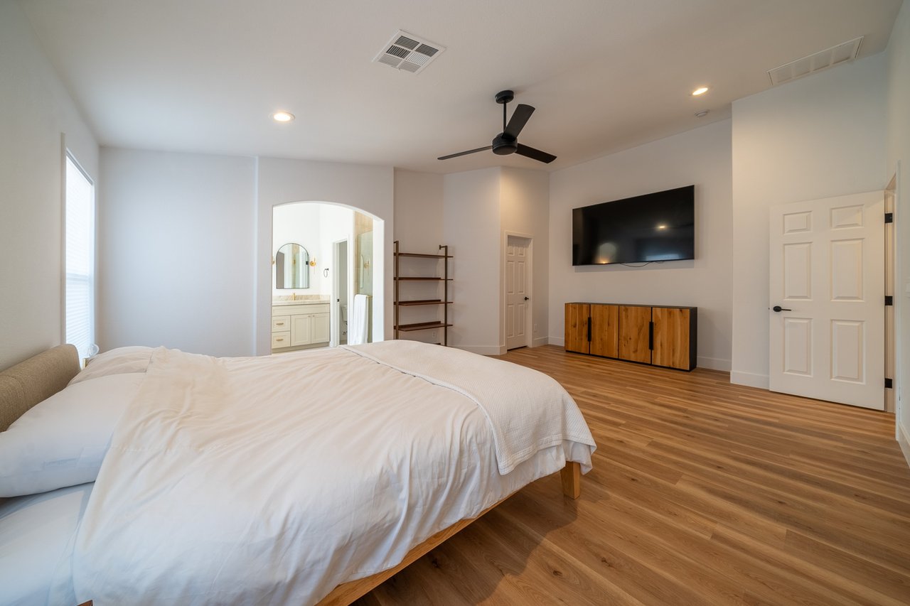 Bedroom with a white bed, wood floors, and an arched opening to the ensuite bathroom.