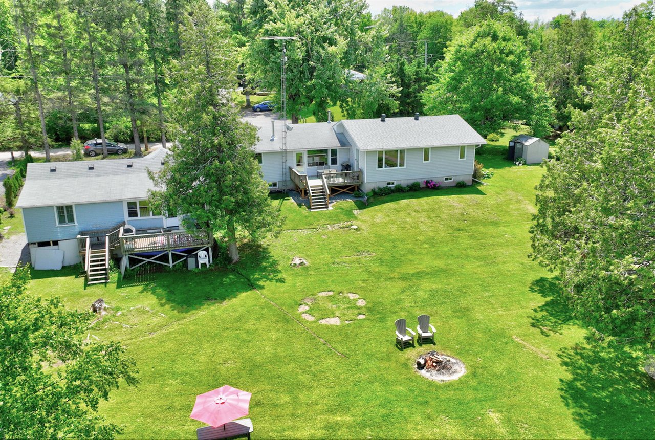Aerial view of two houses and a broad green lawn with decks, Adirondack chairs, and a fire pit.