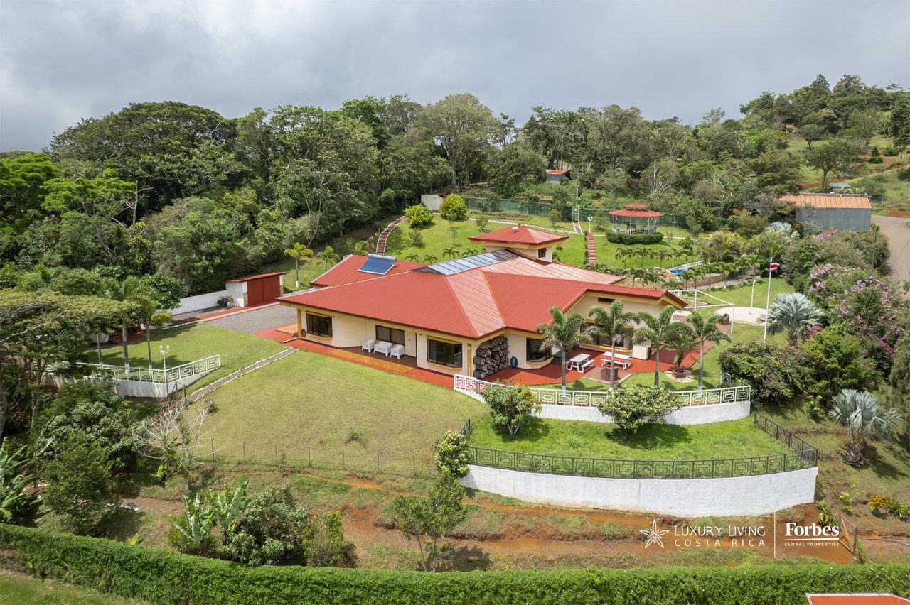 Aerial view of a red-roofed house amid landscaped grounds and dense hillside trees.