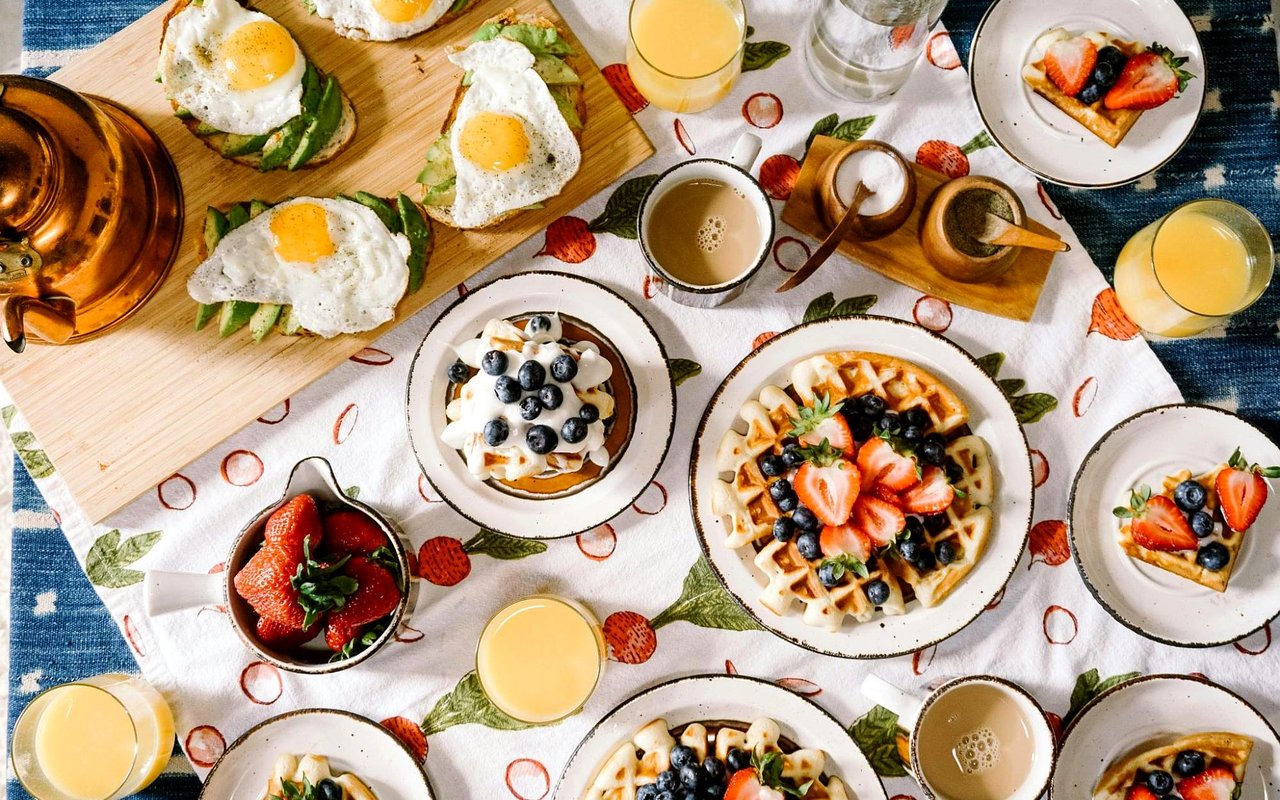 Breakfast spread with egg-topped avocado toast and berry-topped waffles, fruit, coffee, and orange juice.