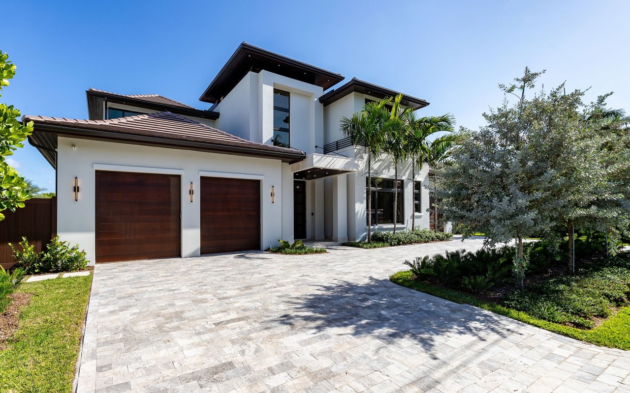 Modern white two-story house with dark wood garage doors and a wide stone-paved driveway.