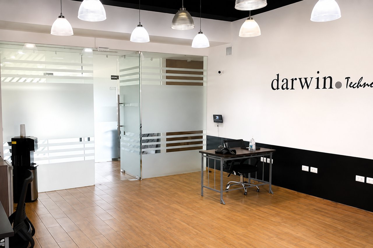 Office reception with frosted-glass partitions, a small desk, pendant lights, and wood-look tile flooring.