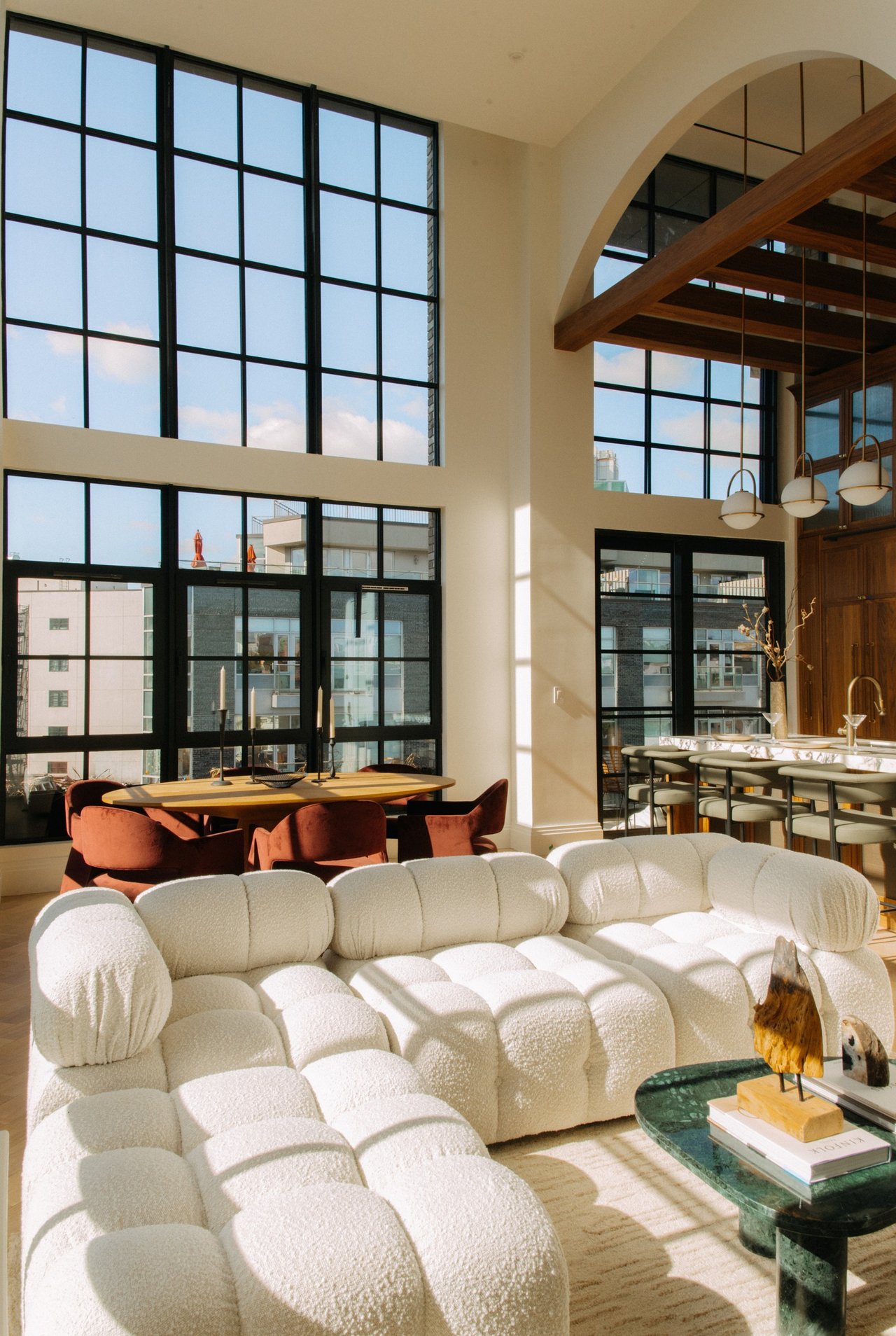 Open-plan living and dining area with a white sectional sofa and tall black-framed windows.