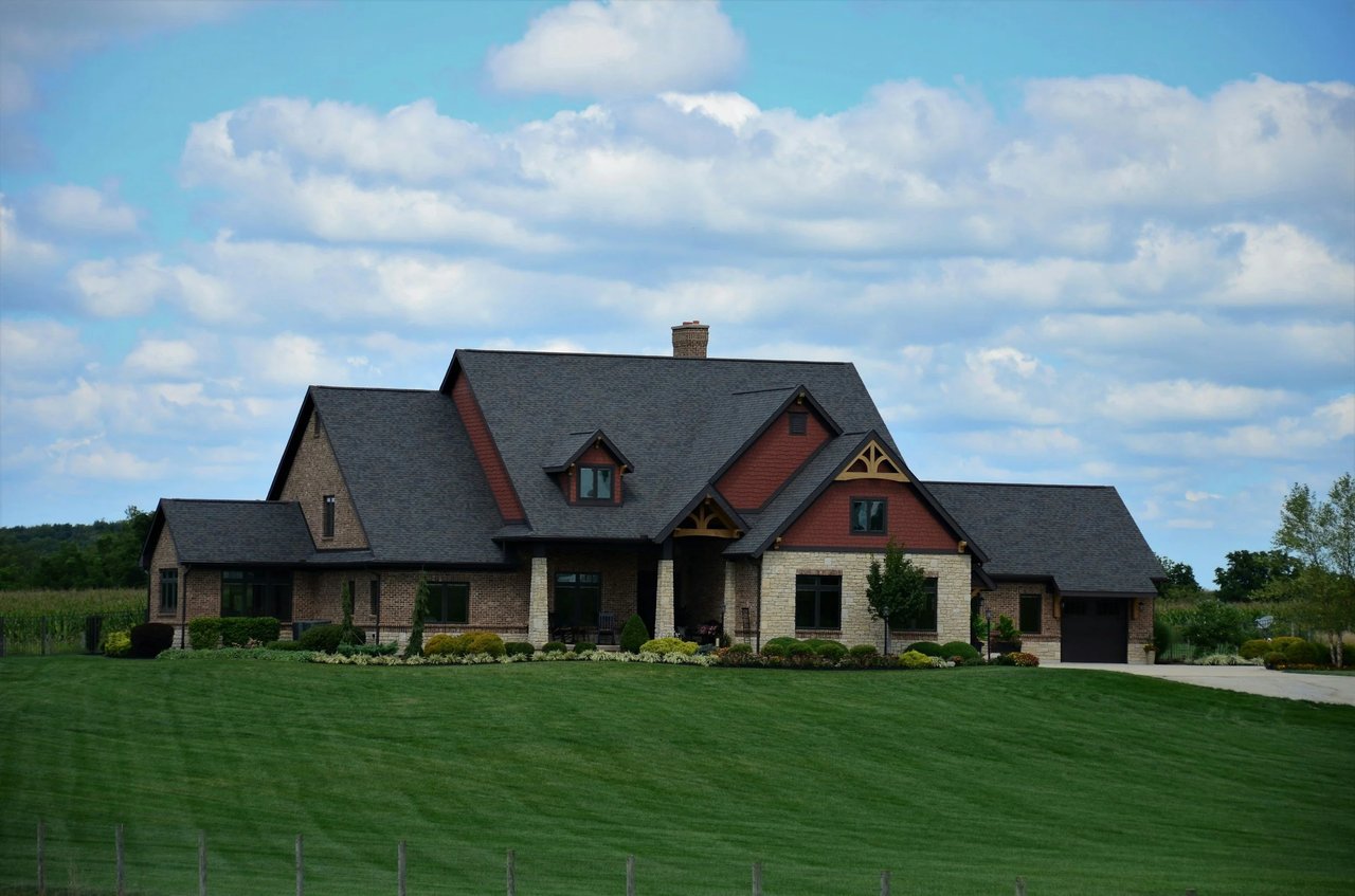Large stone-and-brick home with red gables, an attached garage, and a broad landscaped lawn.