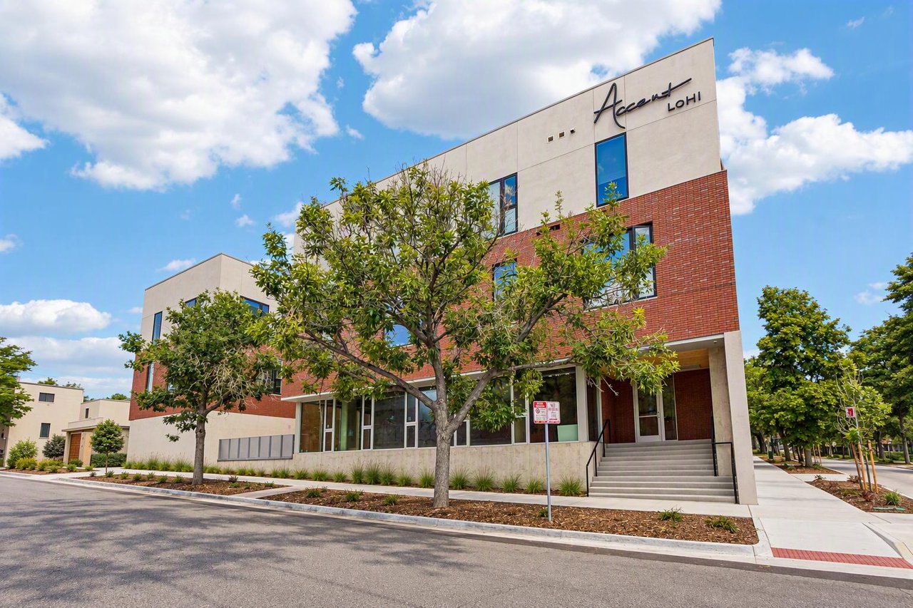 Accent LoHi apartment building with red brick facade, mature trees, and a broad front entrance stairway.