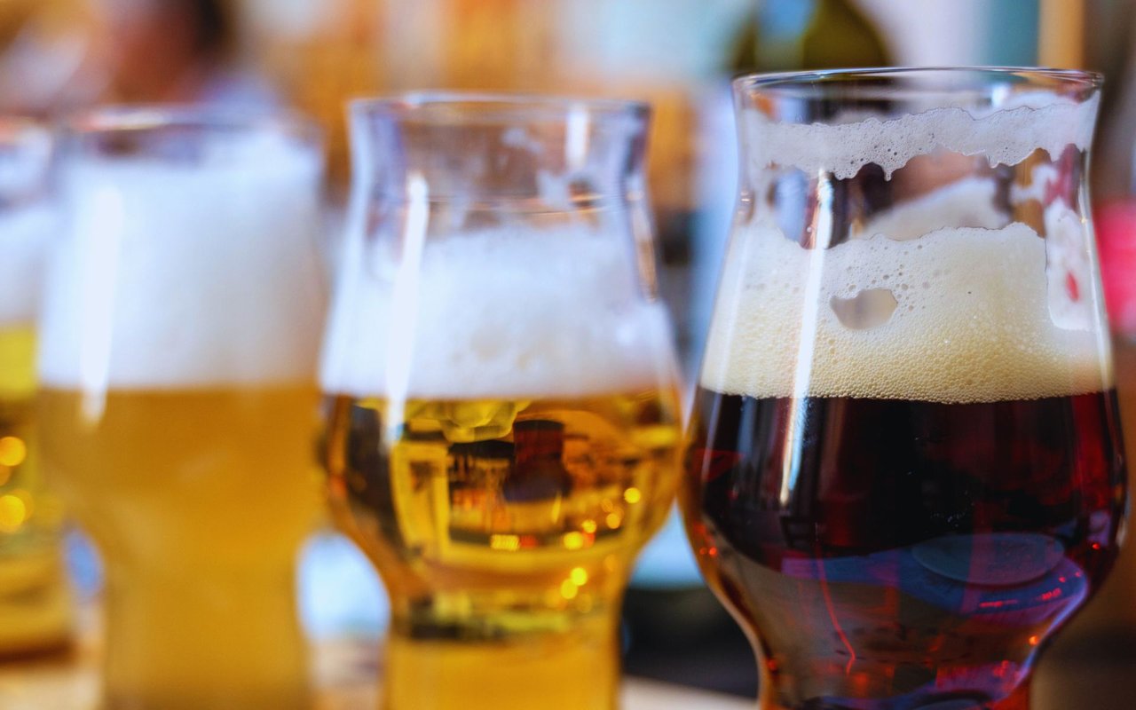 Craft beers in tasting glasses, from golden amber to dark reddish-brown, with a foamy head.