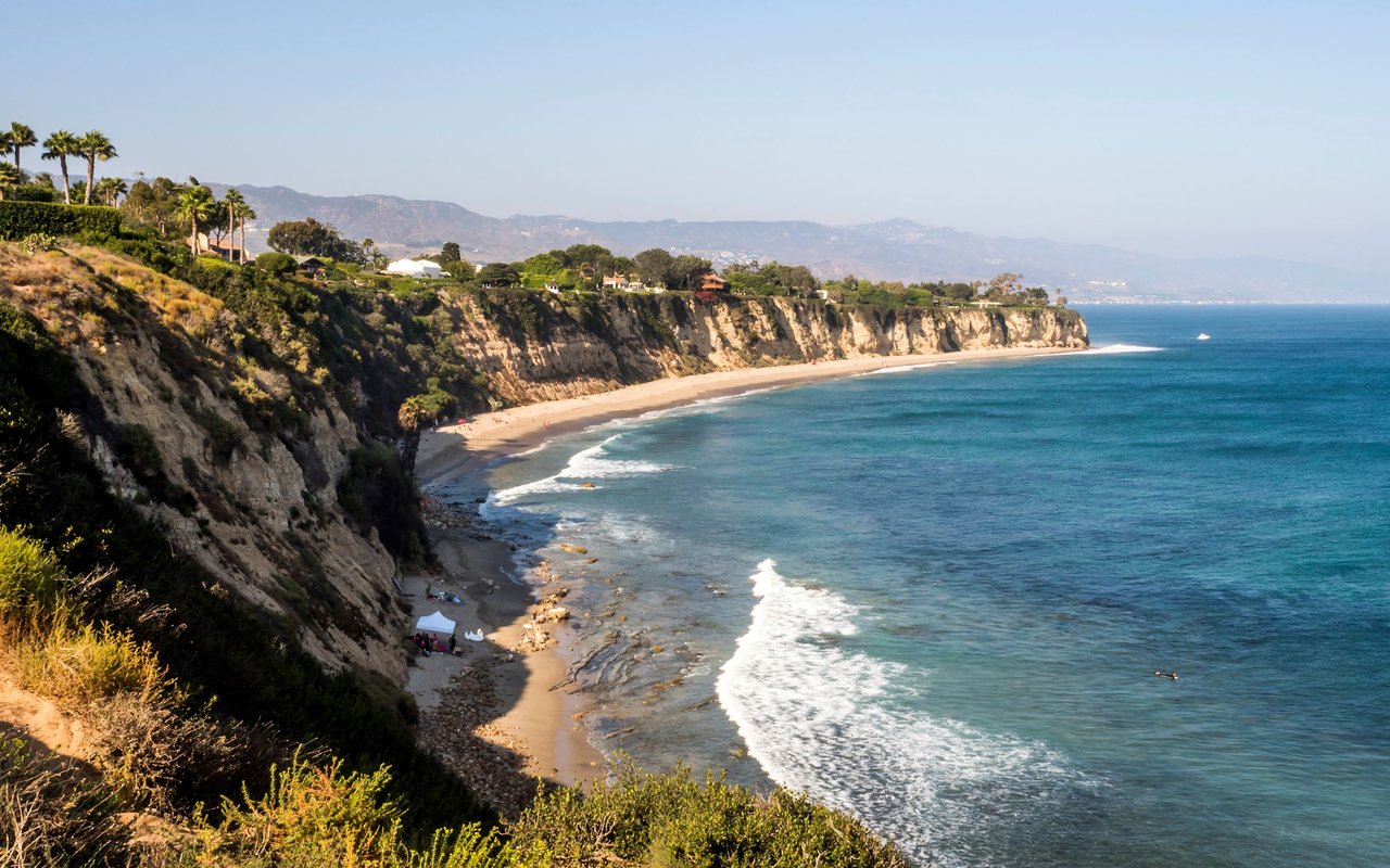 Pacific Palisades coastline with rugged cliffs, a sandy beach, and blue ocean waves.
