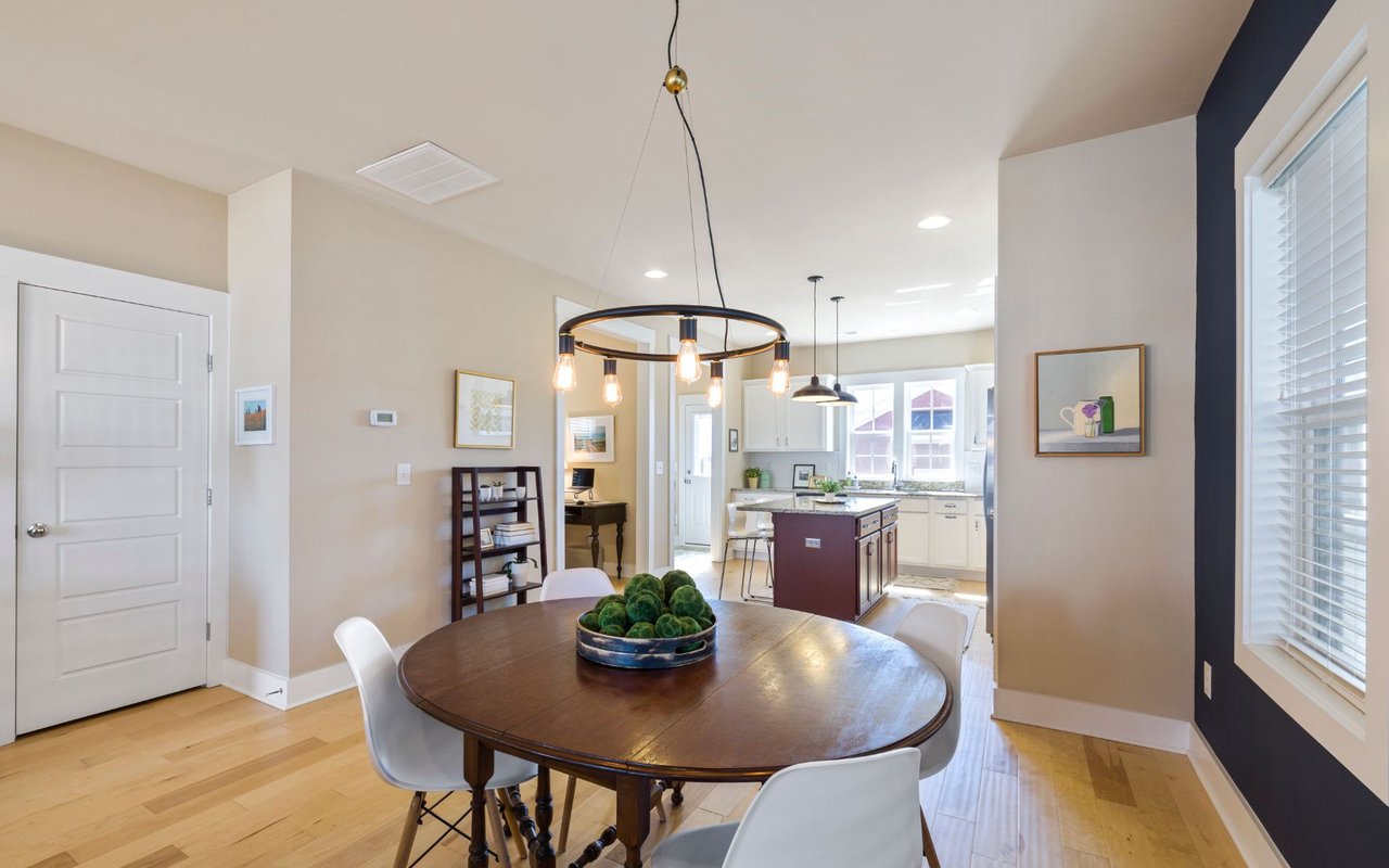Dining area with a round wood table and pendant light, opening into a bright white kitchen.