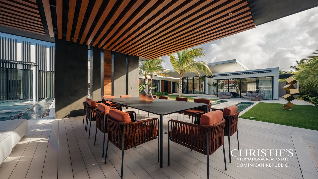 Modern villa’s covered outdoor dining terrace beside a courtyard pool and landscaped lawn.
