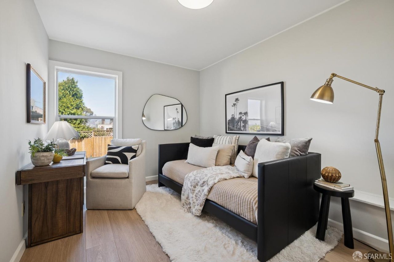 Staged bedroom with a black bed, light bedding, an armchair, and a large window.