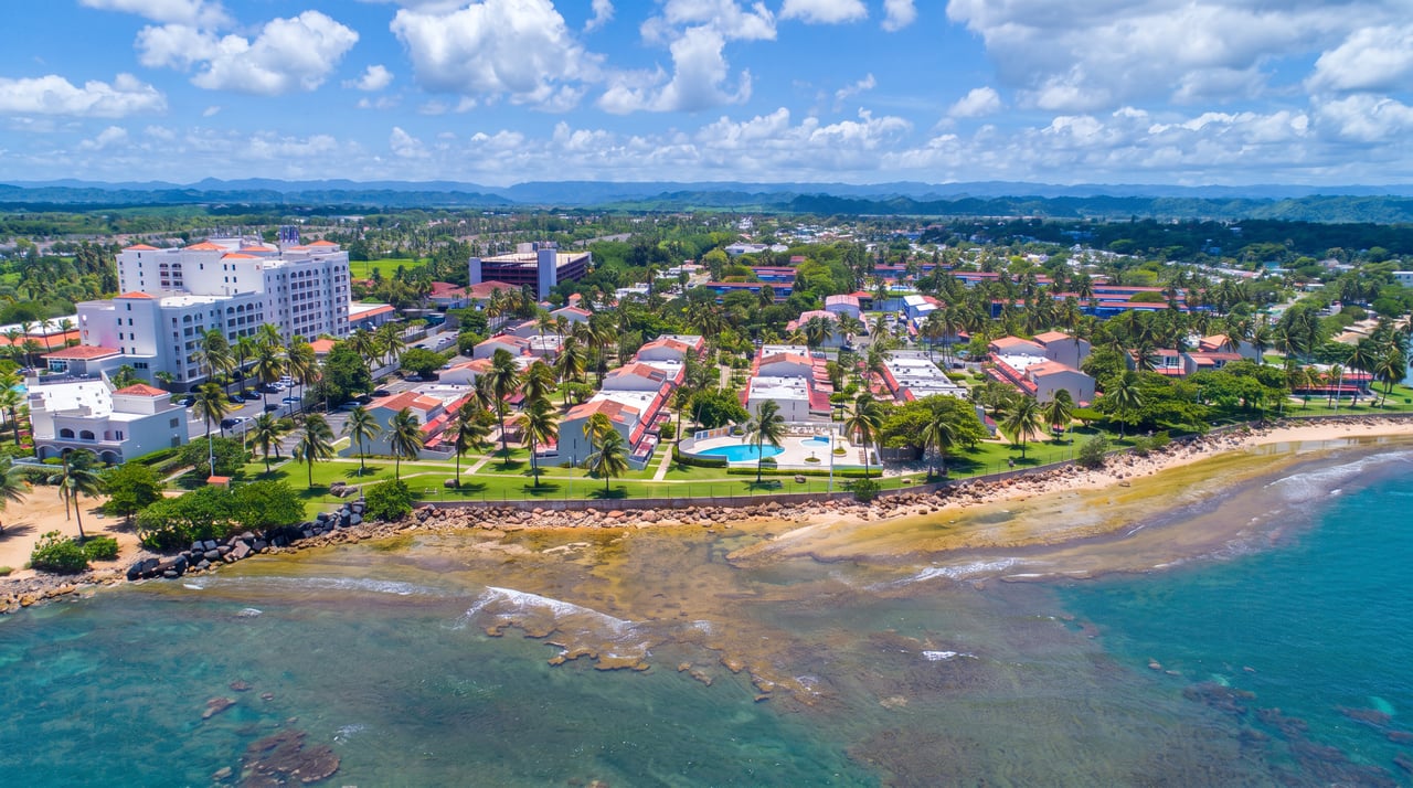 Aerial view of a beachfront villa complex with a pool, palms, and turquoise coastal water.