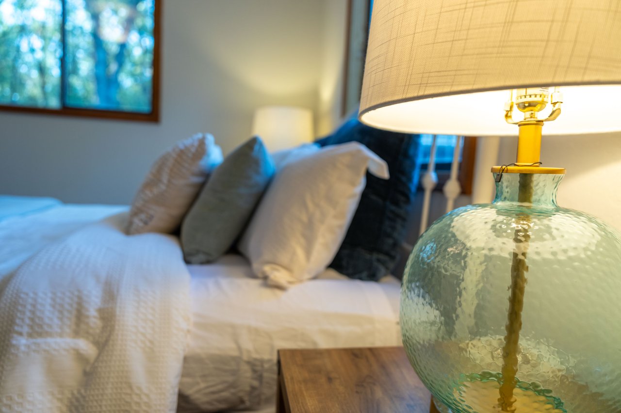 Bedroom with layered neutral pillows and a textured glass bedside lamp.
