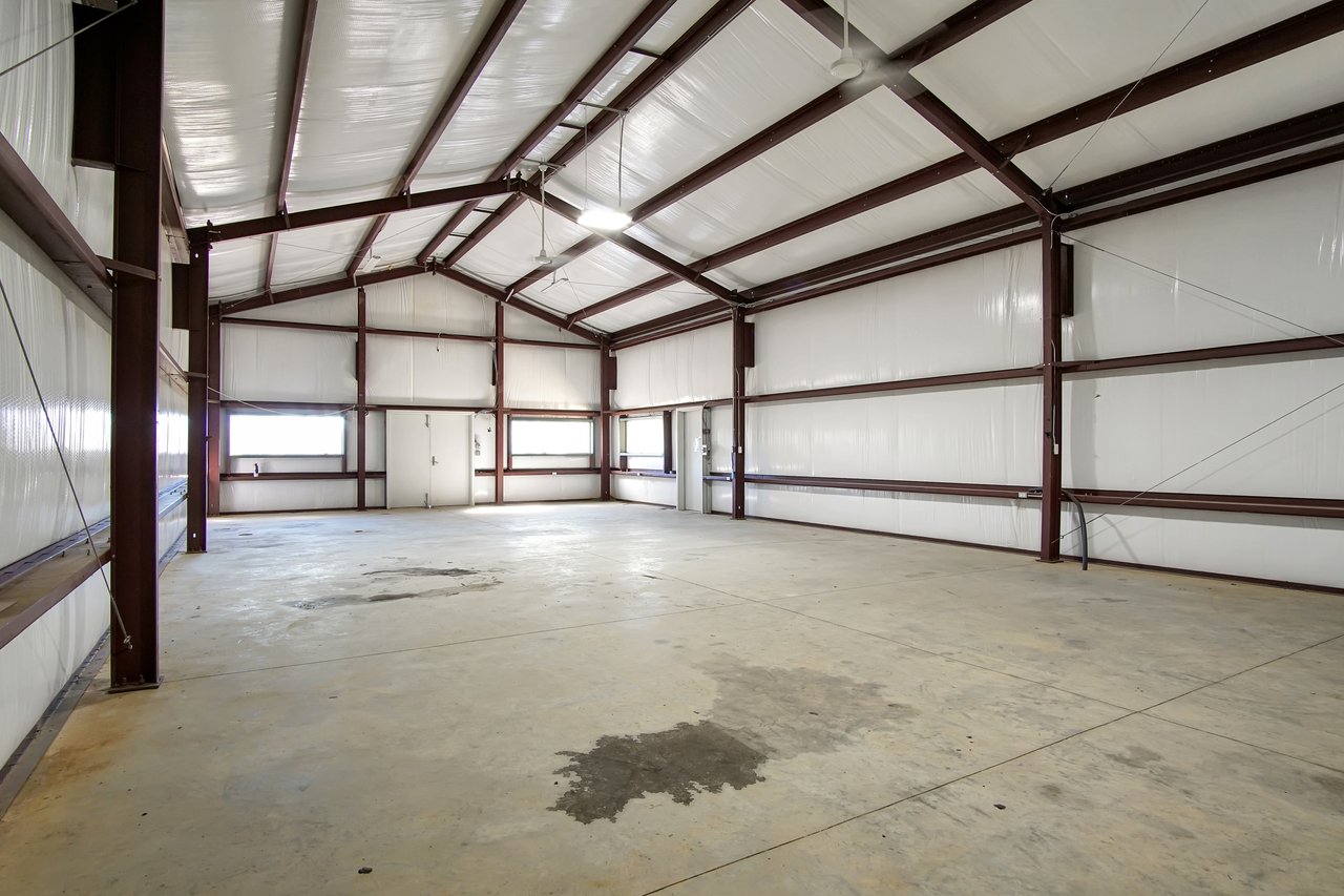 Spacious empty warehouse interior with high ceilings, white walls, steel beams, and concrete floor. Bright lighting and a clean, industrial feel.