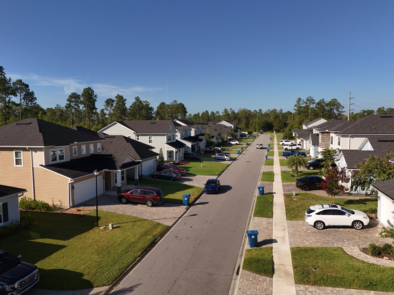 Aerial view down a Holly Forest residential street lined with homes, driveways, sidewalks, and lawns.