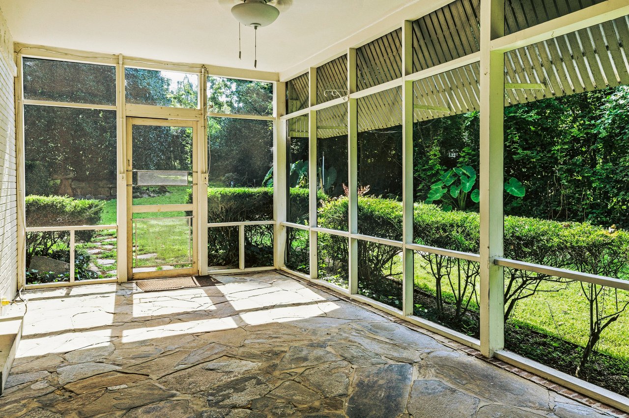 Screened porch with a flagstone floor and lush garden views.