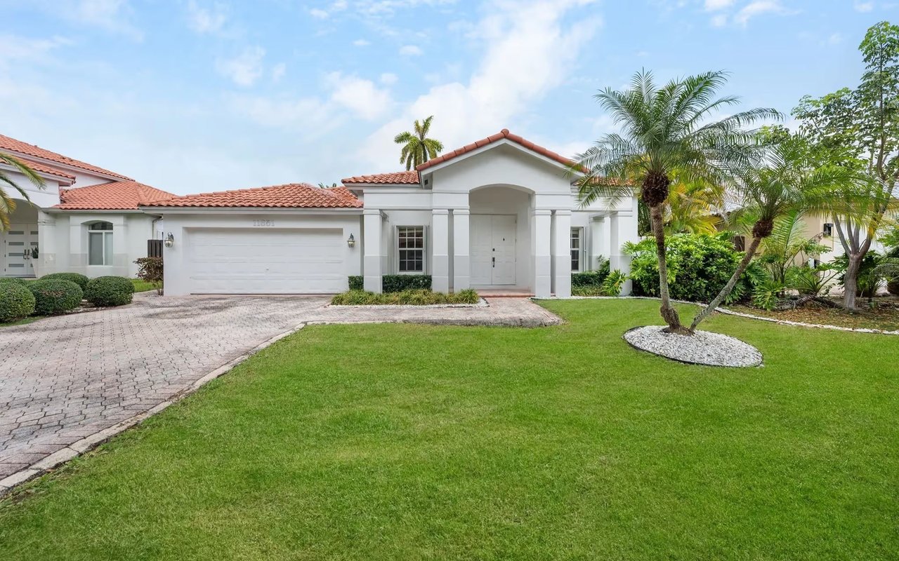 White stucco home with a red tile roof, arched entry, two-car garage, and palm-lined lawn.