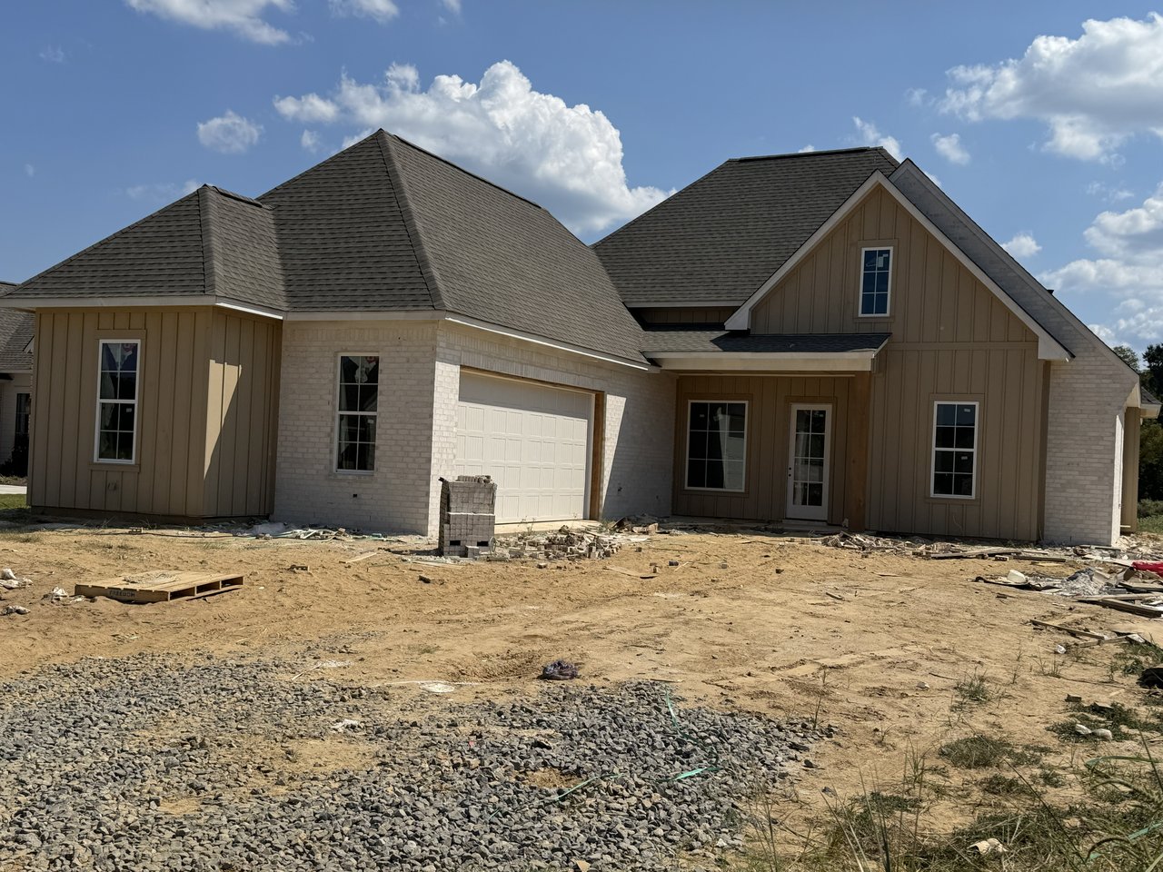 Newly constructed tan home with brick accents, an attached garage, and an unfinished dirt yard.