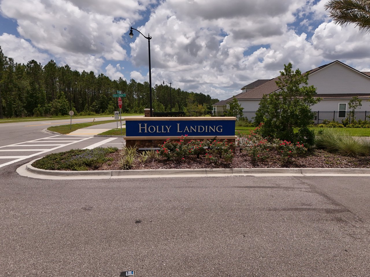 Holly Landing entrance sign beside landscaped flower beds and neighborhood homes.