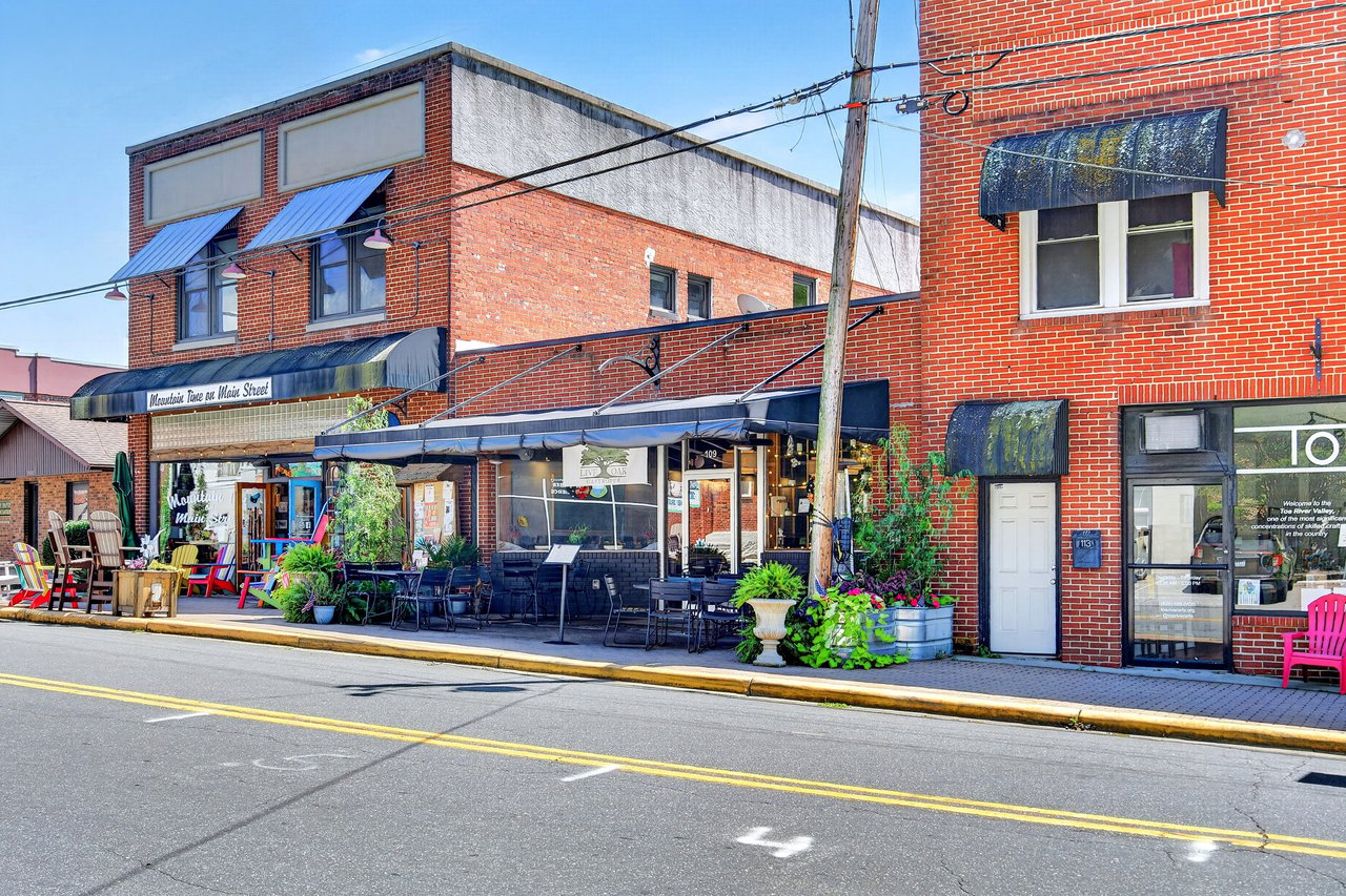 Brick restaurant storefront with blue awnings, outdoor patio seating, and planters along a downtown street.