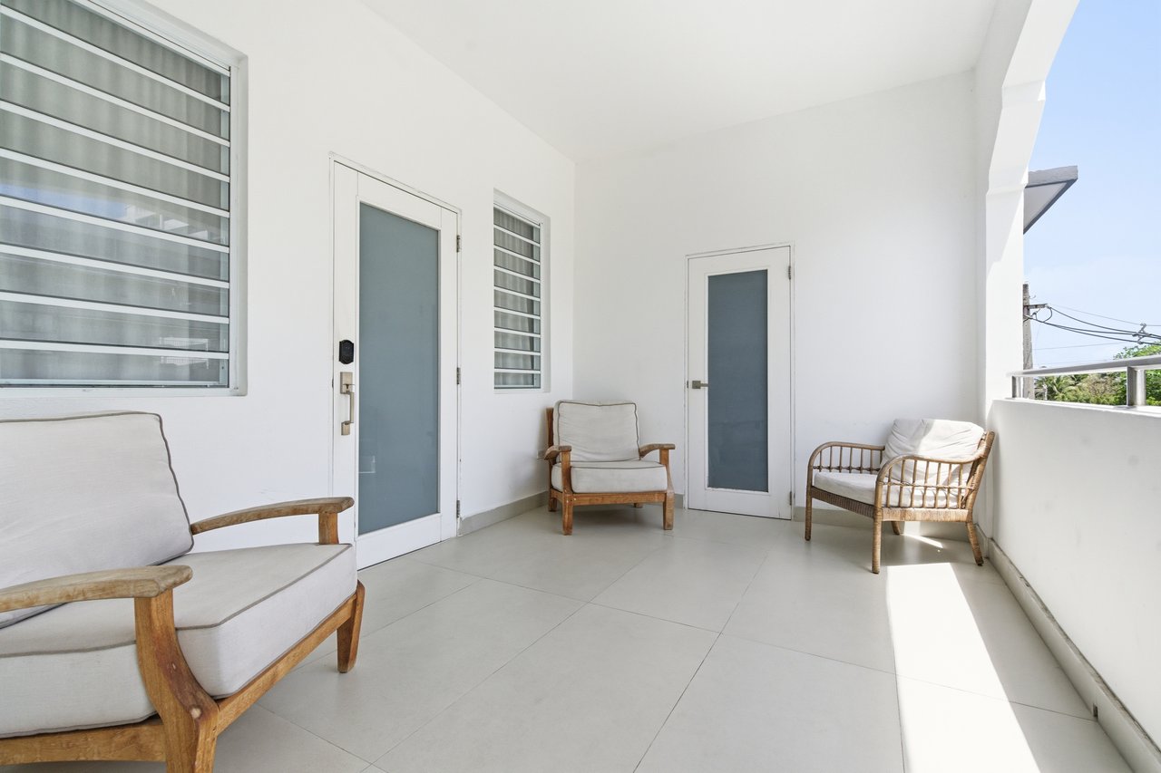 Covered balcony with pale tile flooring, frosted-glass doors, louvered windows, and three cushioned wooden chairs.