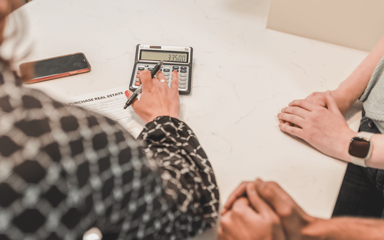 People review real estate purchase paperwork and calculate costs at a table.