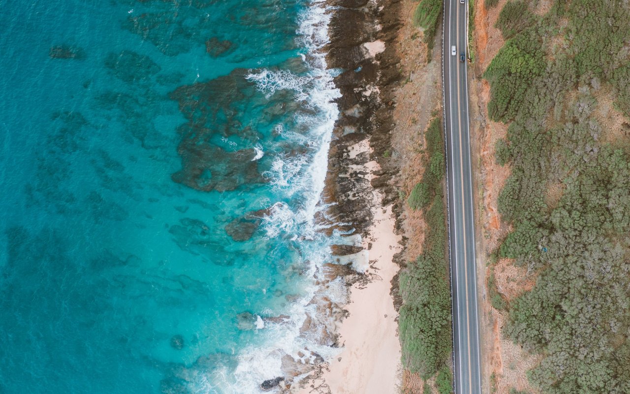 Coastal highway beside turquoise water, rocky shore, and a narrow sandy beach.