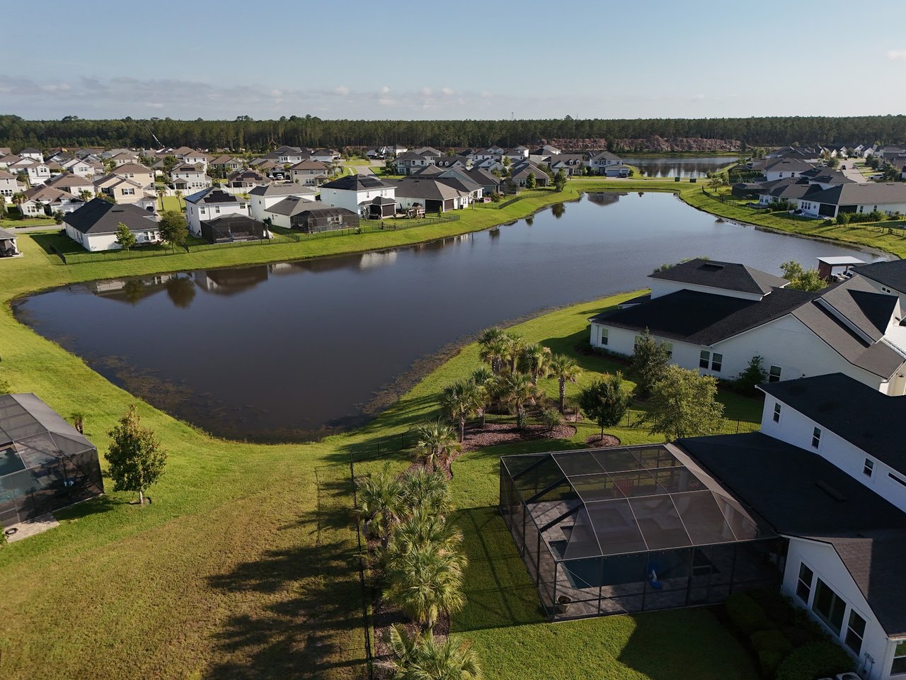 Aerial view of homes around a pond, with green lawns and screened pool enclosures.